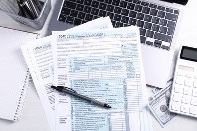 Tax forms, money, stationery, laptop and calculator on light grey table, flat lay