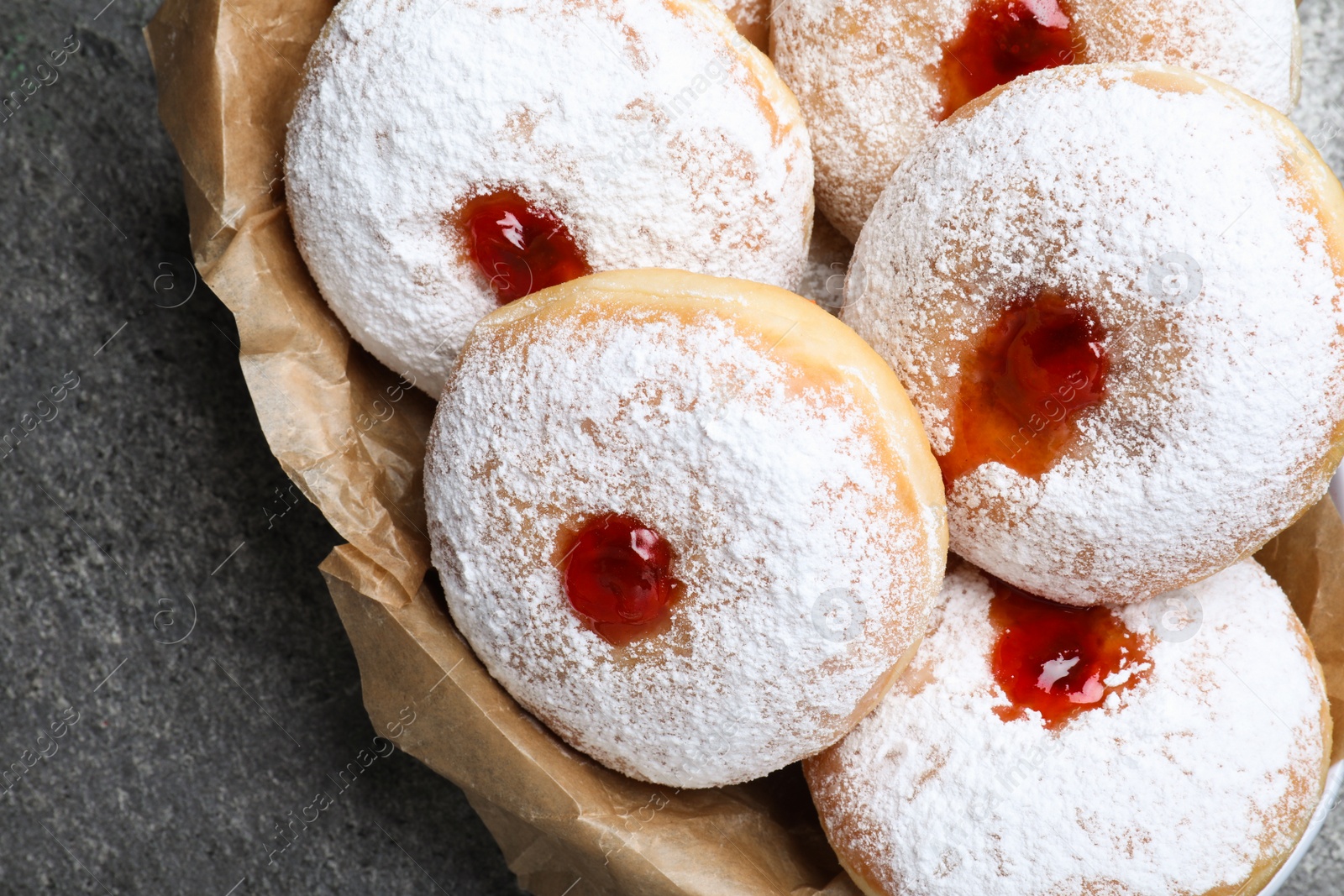 Photo of Delicious donuts with jelly and powdered sugar in bowl on grey table, closeup