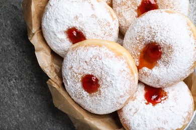 Photo of Delicious donuts with jelly and powdered sugar in bowl on grey table, closeup