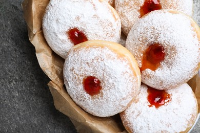 Delicious donuts with jelly and powdered sugar in bowl on grey table, closeup