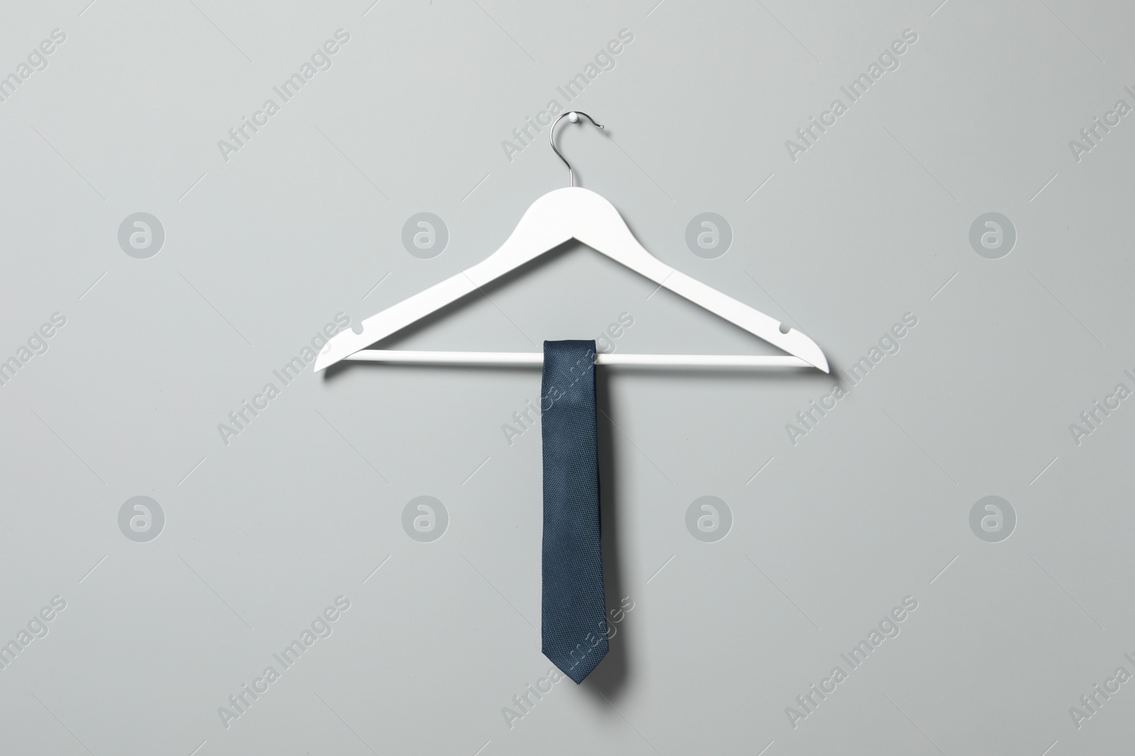 Photo of Hanger with blue necktie on light grey wall