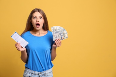 Portrait of emotional young woman with lottery ticket and money on yellow background, space for text