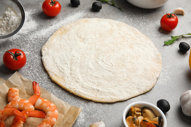 Photo of Dough and fresh ingredients for seafood pizza on grey table