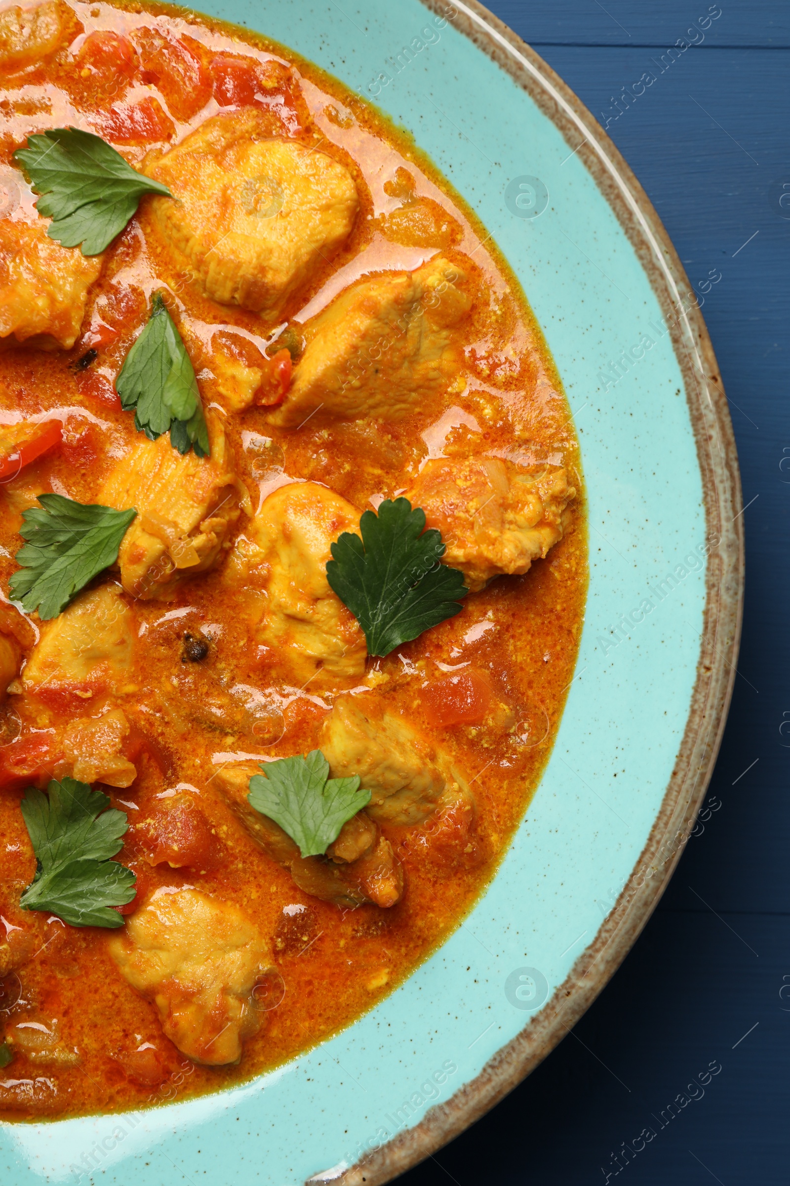 Photo of Delicious chicken curry on blue wooden table, top view