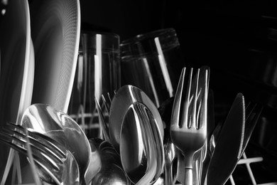 Photo of Clean plates and cutlery in dishwasher, closeup