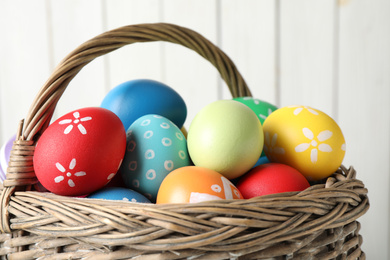 Photo of Colorful Easter eggs in wicker basket against light background, closeup