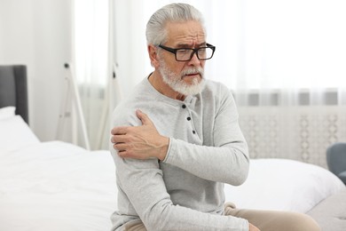 Photo of Arthritis symptoms. Man suffering from pain in shoulder on bed at home