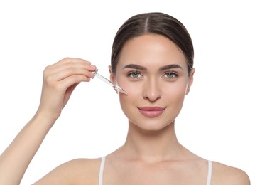 Young woman applying essential oil onto face on white background