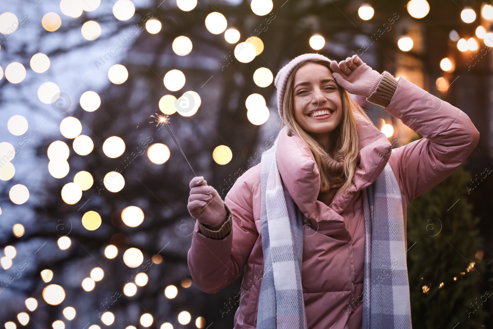 Photo of Happy young woman with sparkler on city street in evening. Christmas celebration