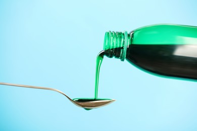 Photo of Pouring cough syrup into spoon on turquoise background