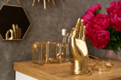 Golden hand shaped holder, jewelry and accessories on dressing table near grey wall. Space for text