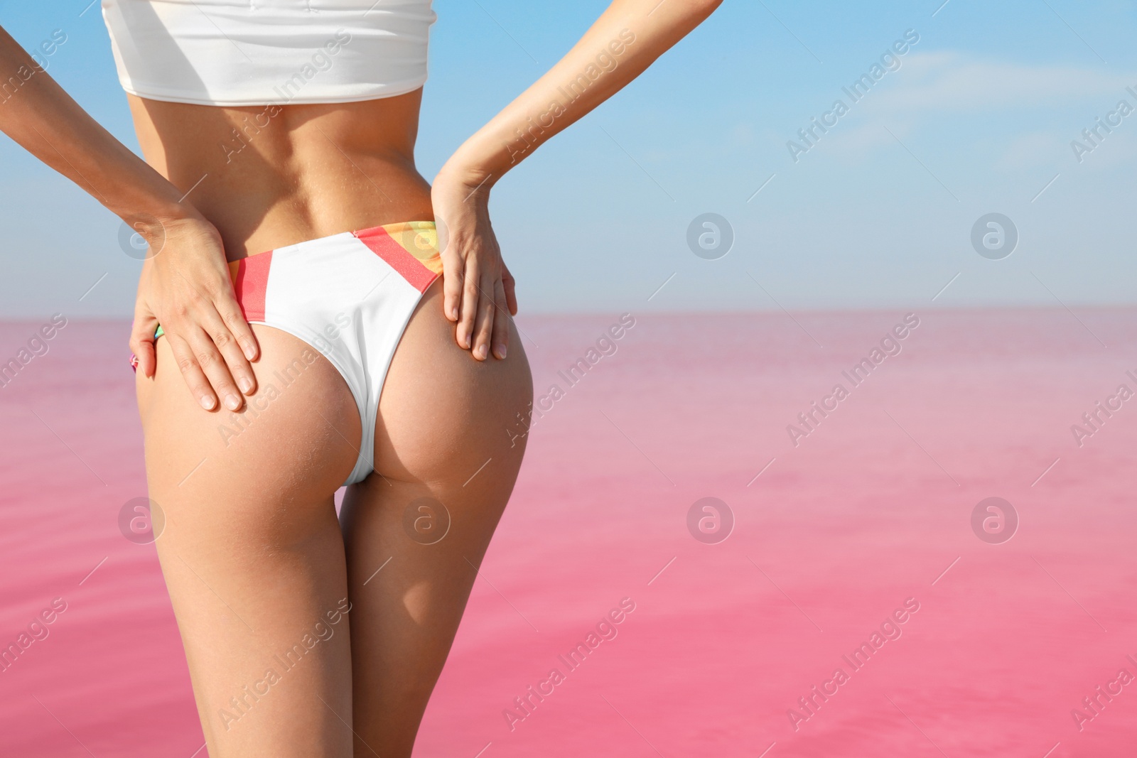 Photo of Beautiful woman in swimsuit posing near pink lake on sunny day, closeup