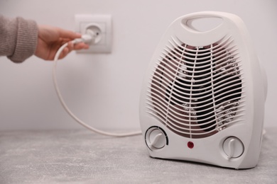 Photo of Woman plug in modern electric fan heater indoors, focus on device. Space for text