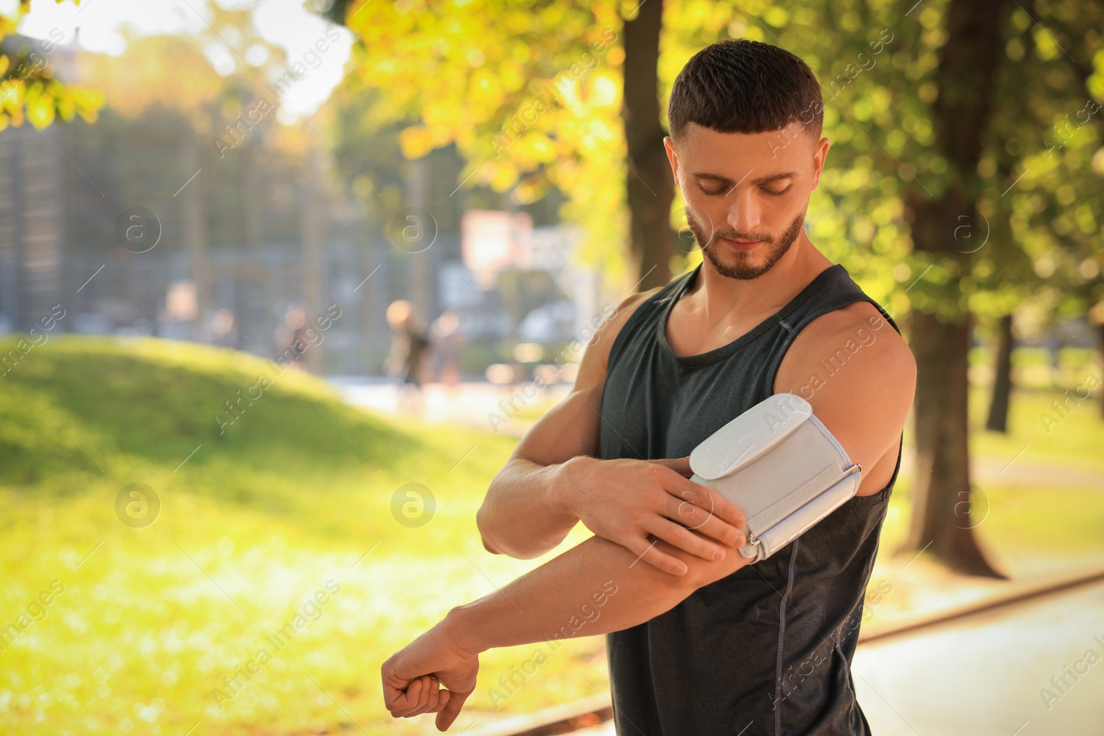 Photo of Attractive serious man checking blood pressure with modern monitor after training in park on sunny day. Space for text