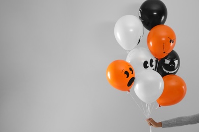 Woman holding color balloons for Halloween party on light grey background, closeup. Space for text