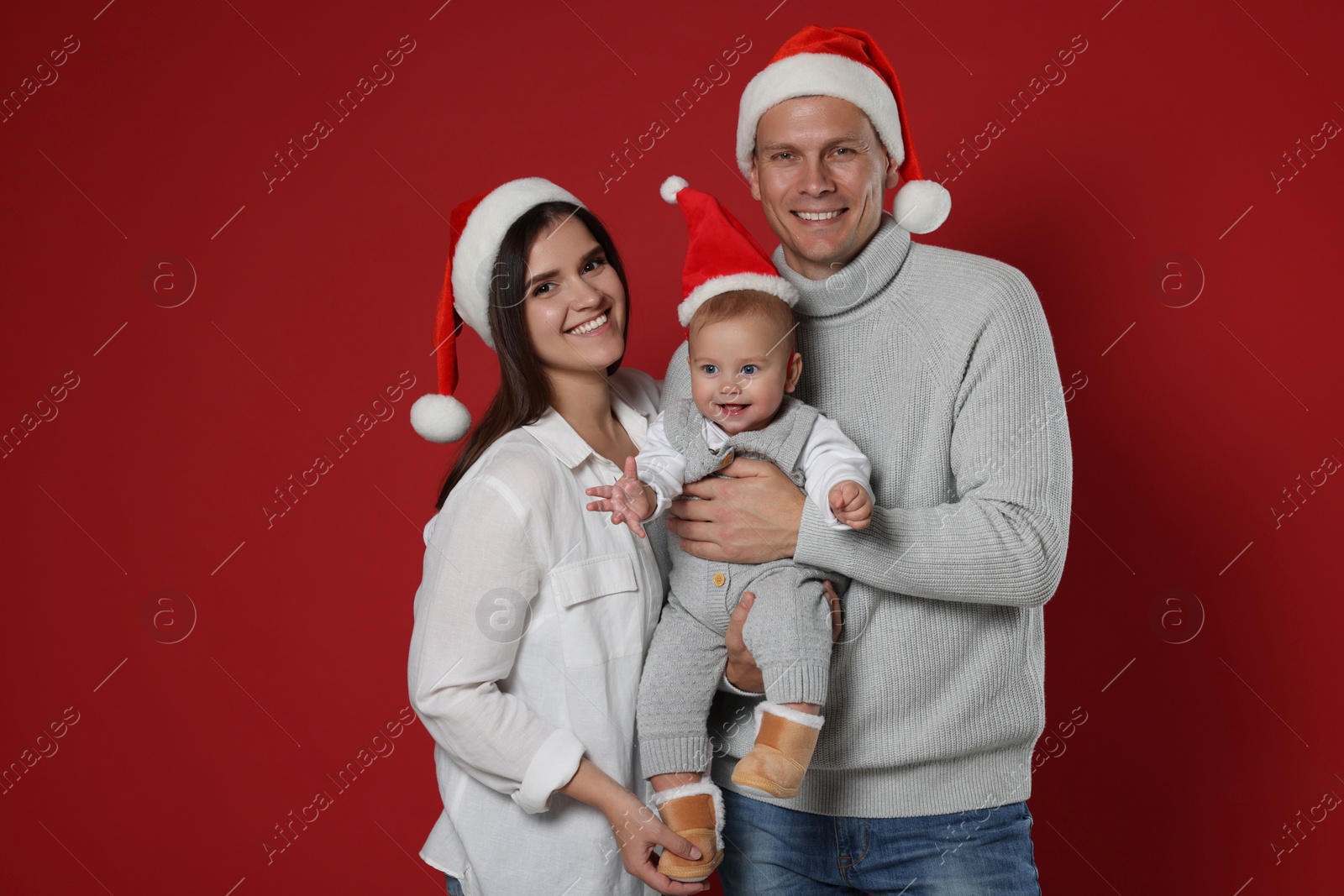 Photo of Happy couple with cute baby wearing Santa hats on red background. Christmas season