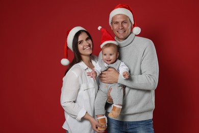 Photo of Happy couple with cute baby wearing Santa hats on red background. Christmas season