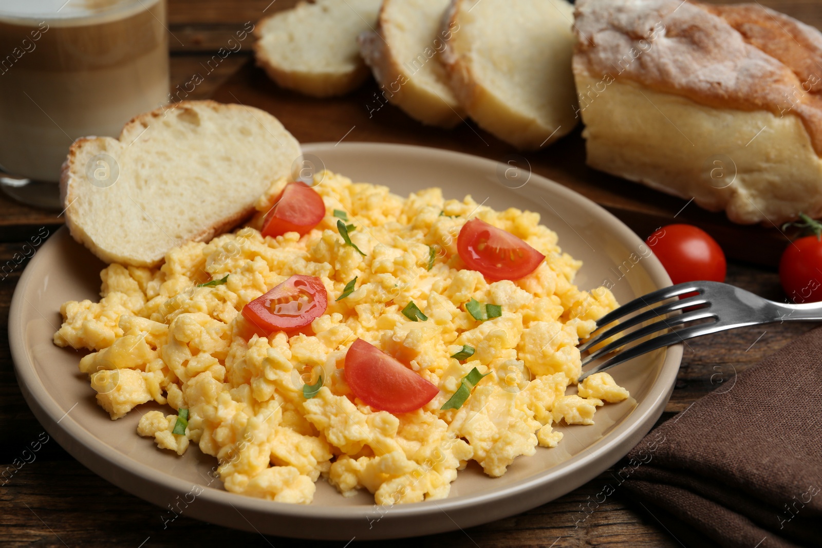 Photo of Tasty scrambled eggs with cherry tomato and bread on wooden table, closeup