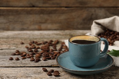 Photo of Cup of aromatic hot coffee and beans on wooden table, space for text