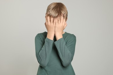 Boy covering face with hands on light grey background. Children's bullying