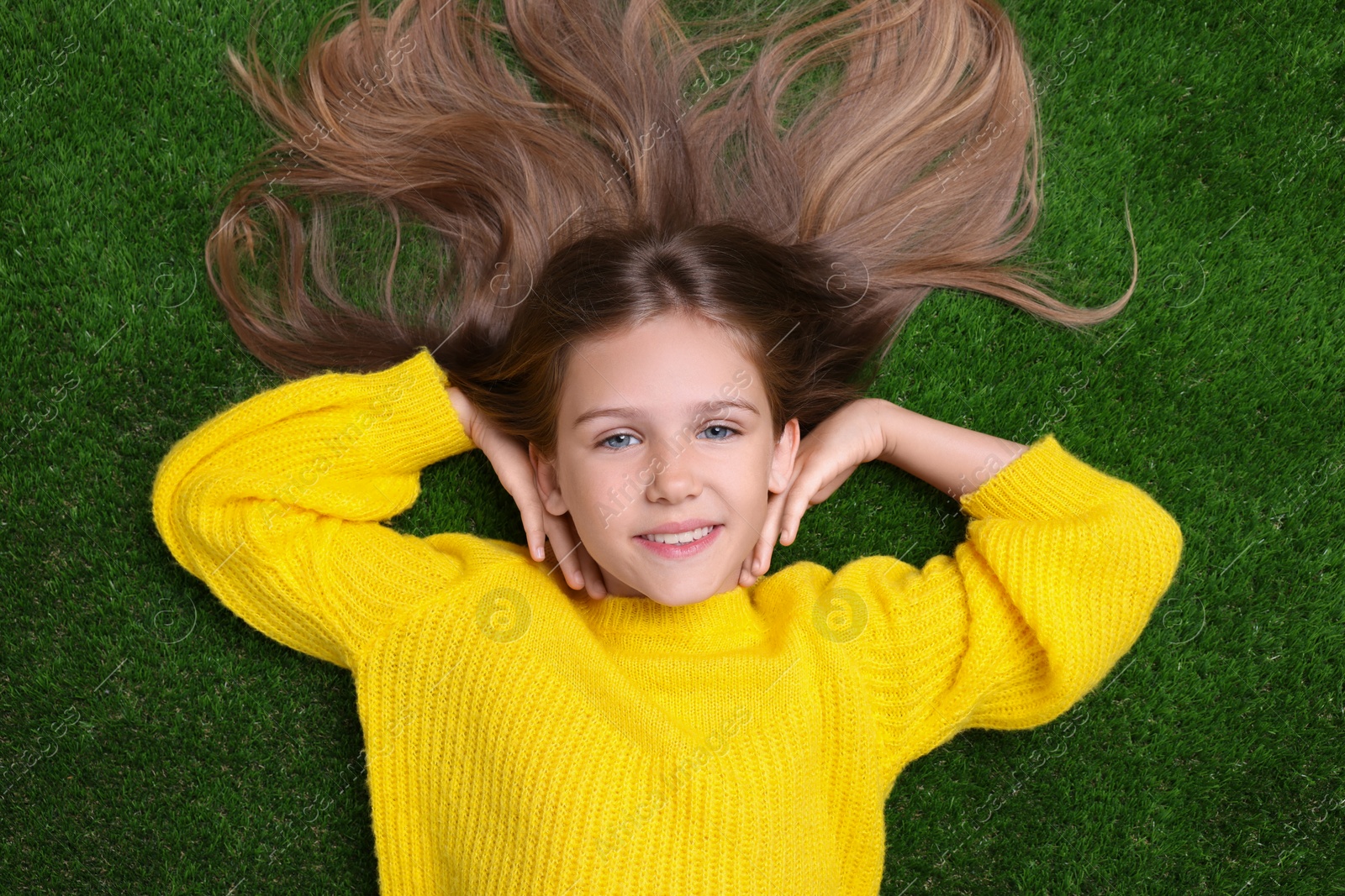 Photo of Little smiling girl on green grass, top view