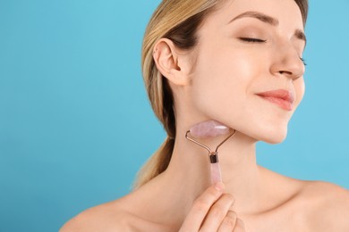 Young woman using natural rose quartz face roller on light blue background, space for text