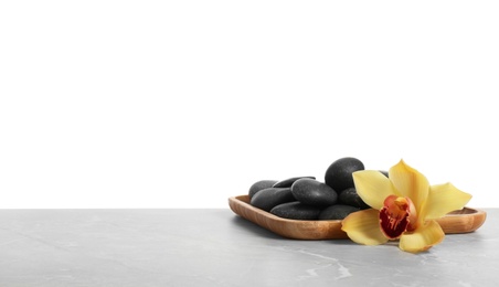 Wooden plate with orchid flower and spa stones on table against white background. Space for text