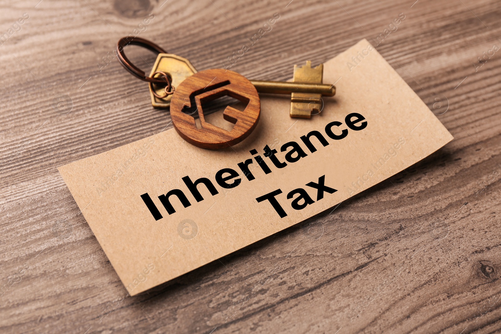 Photo of Inheritance Tax. Card and key with key chain in shape of house on wooden table, closeup