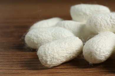 Photo of Heap of white silk cocoons on wooden table, closeup
