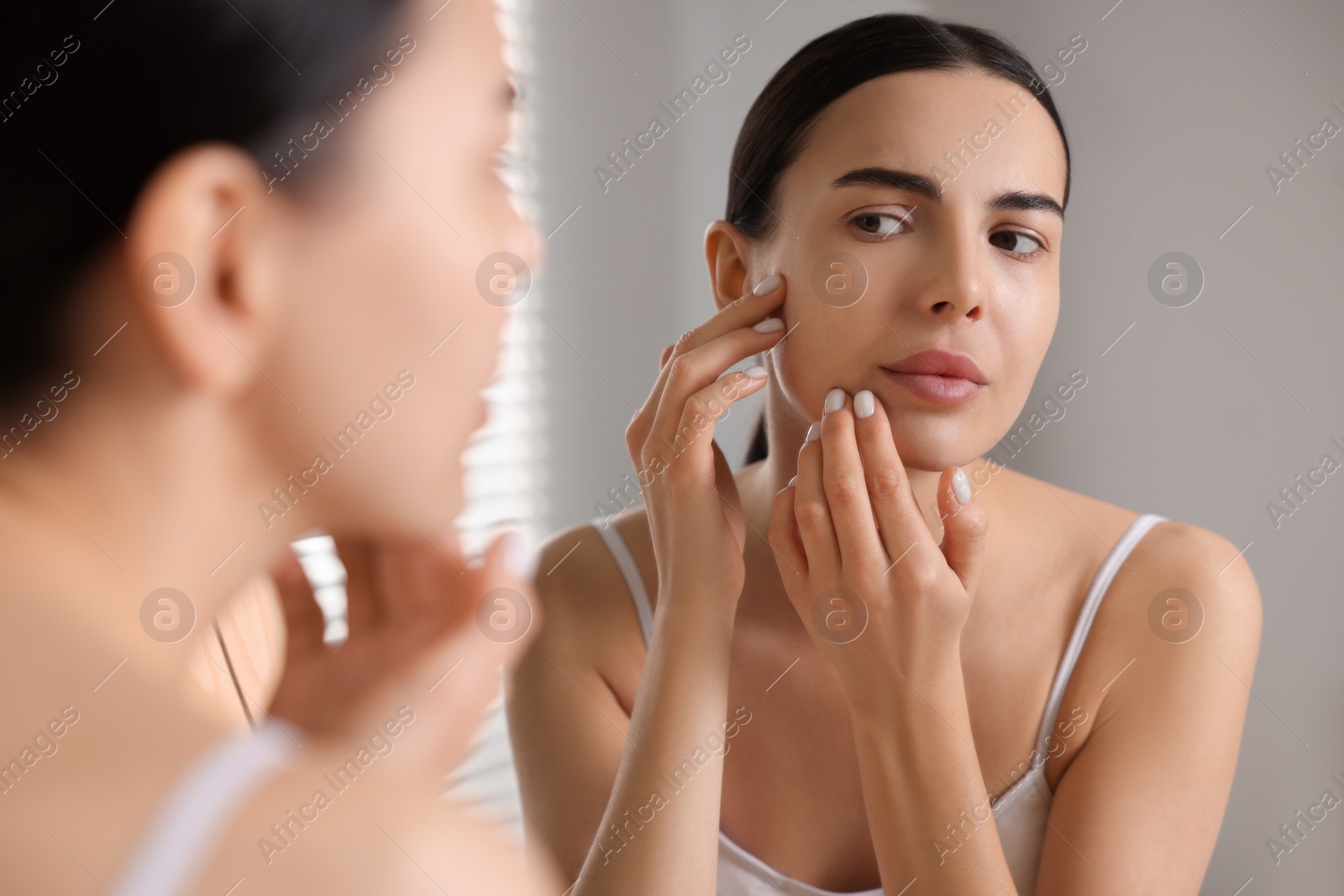 Photo of Woman with dry skin looking at mirror in bathroom