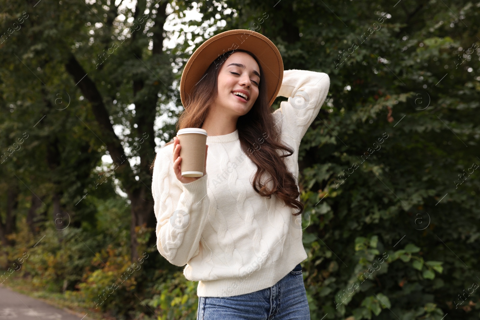 Photo of Beautiful young woman in stylish warm sweater holding paper cup of coffee outdoors