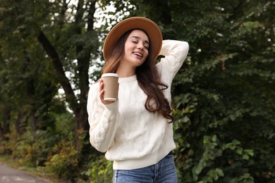 Beautiful young woman in stylish warm sweater holding paper cup of coffee outdoors