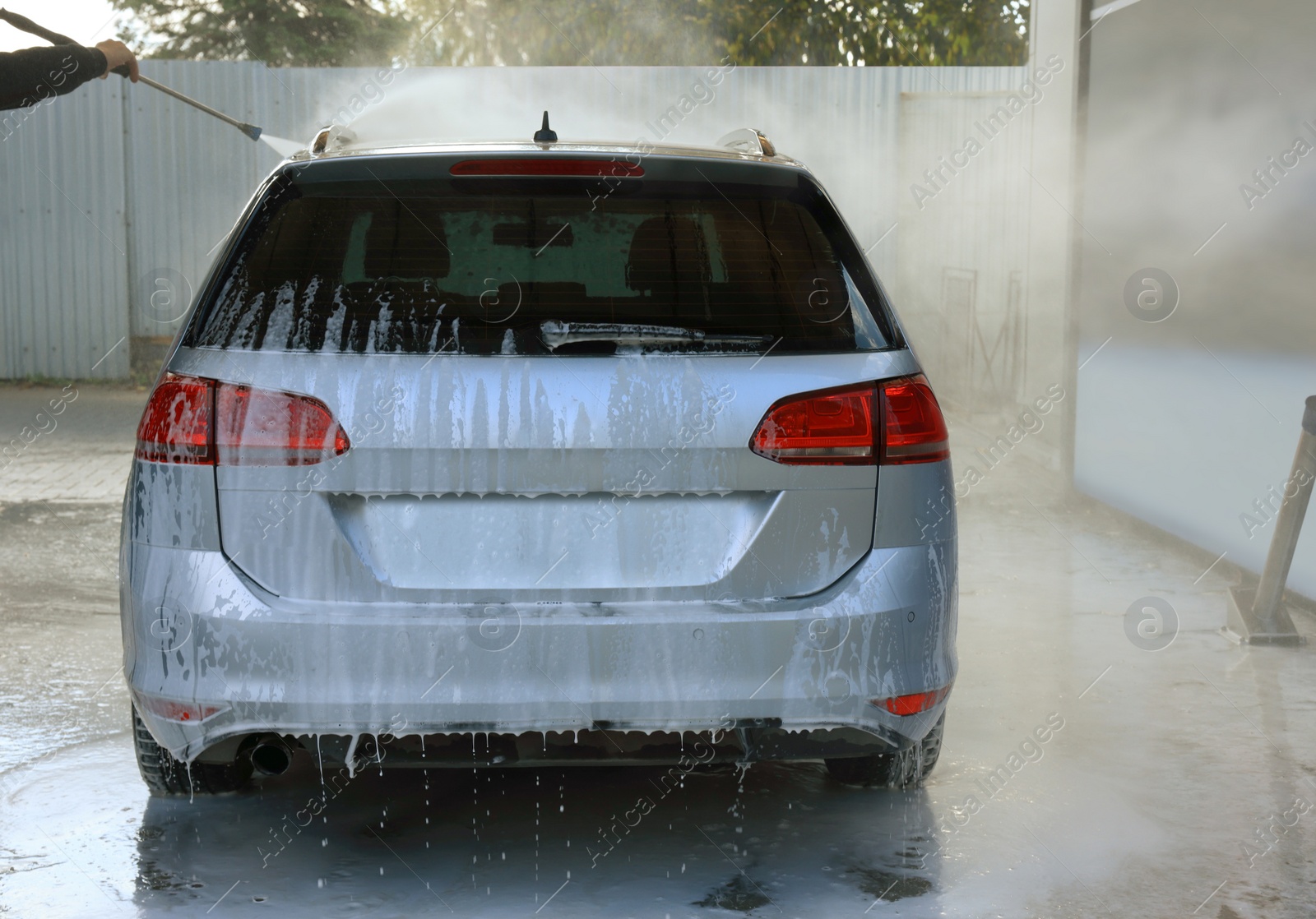 Photo of Man washing auto with high pressure water jet at outdoor car wash, closeup