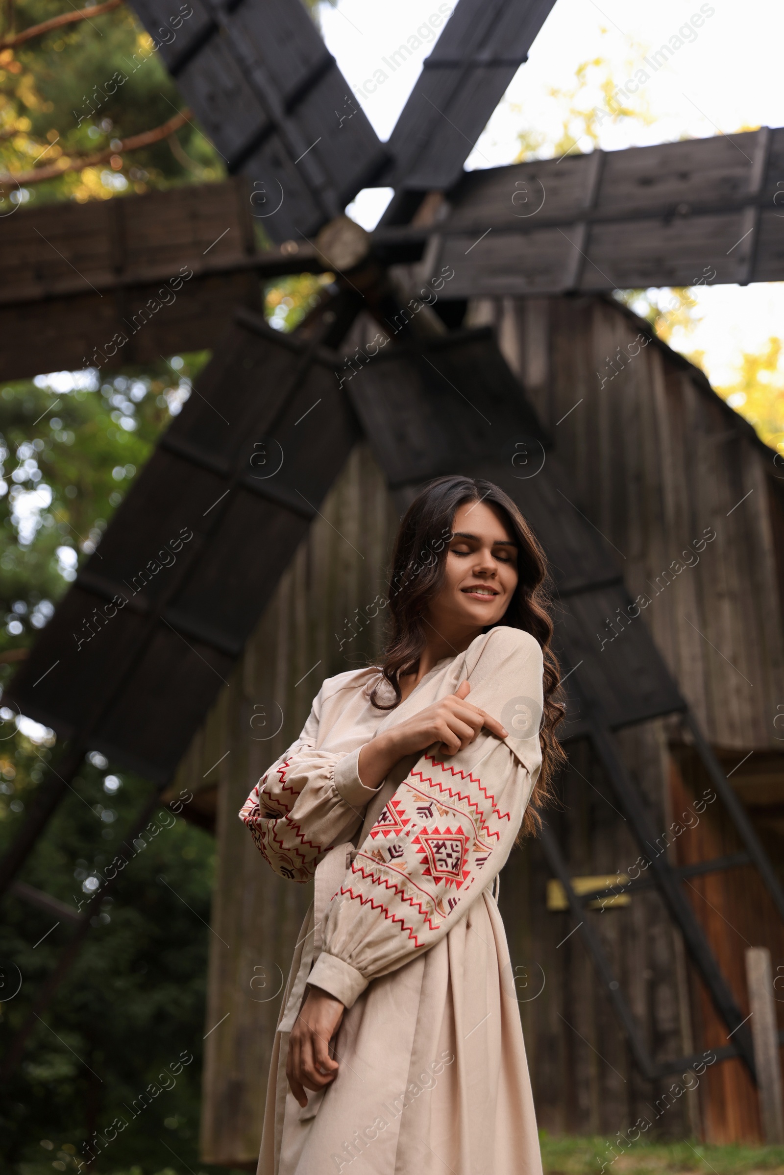 Photo of Beautiful woman wearing embroidered dress near old wooden mill in countryside. Ukrainian national clothes