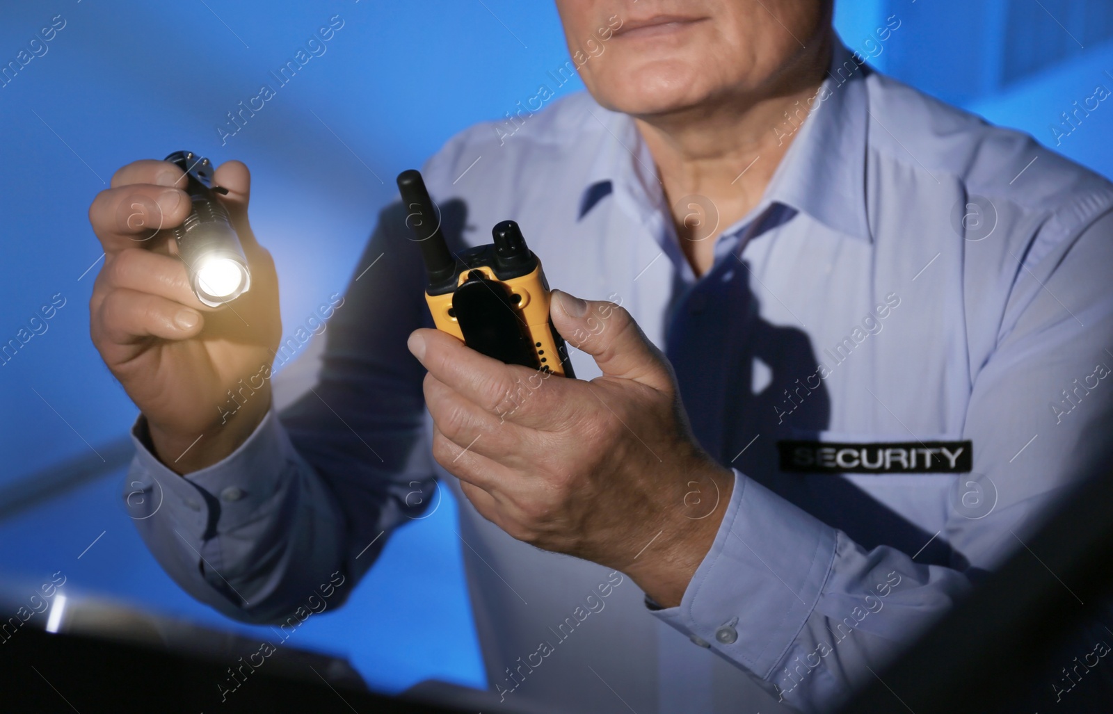 Photo of Professional security guard with portable radio set and flashlight in dark room, closeup