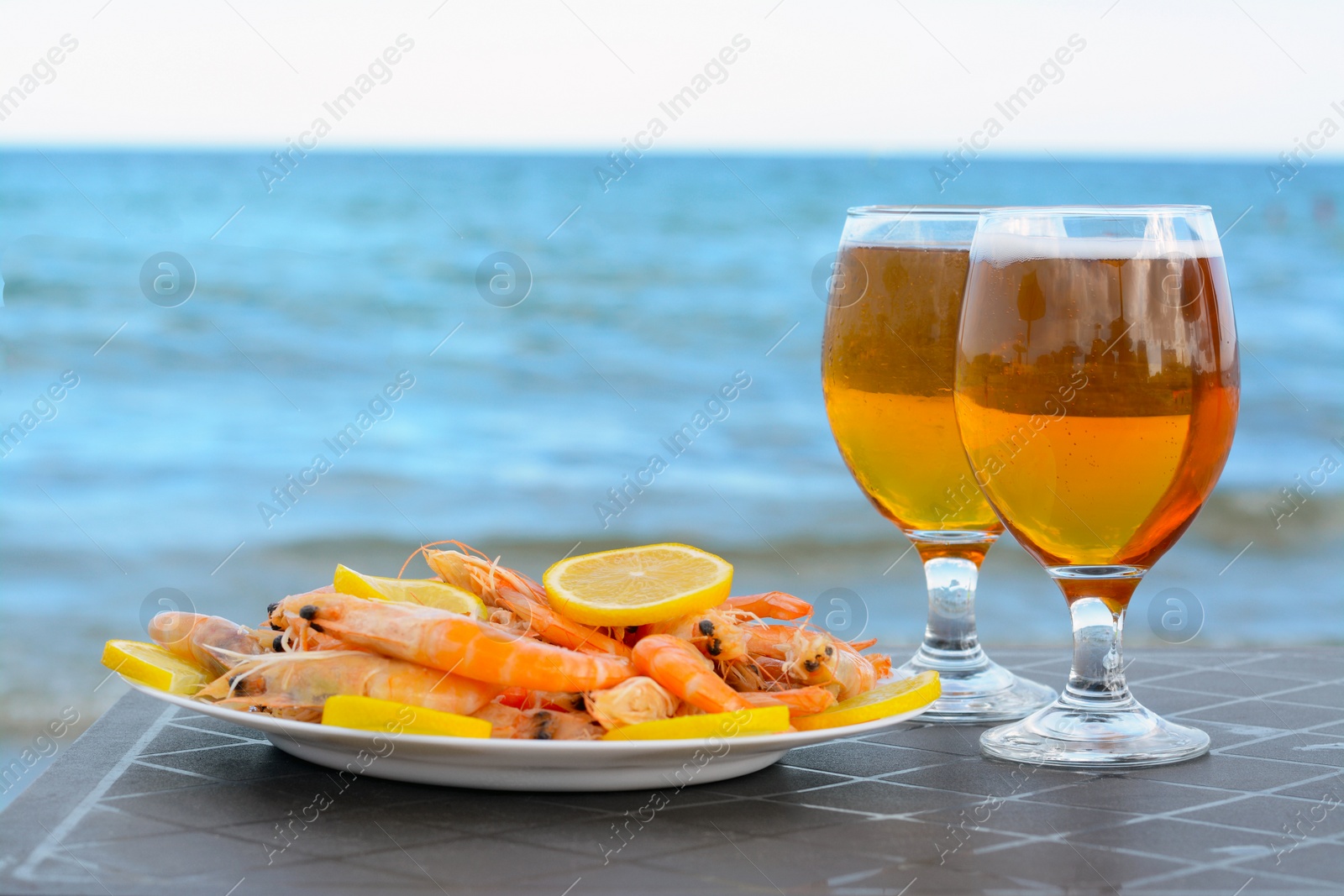 Photo of Cold beer in glasses and shrimps served with lemon on beach