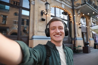 Photo of Smiling man in headphones taking selfie outdoors