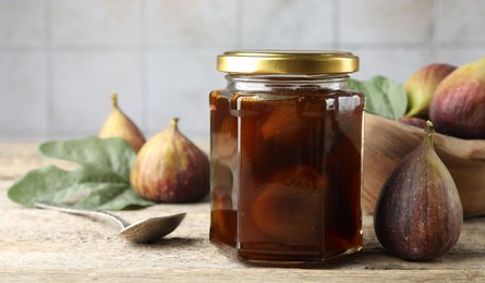 Photo of Jar of tasty sweet jam and fresh figs on wooden table. Space for text
