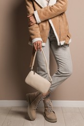 Photo of Fashionable woman with stylish bag near beige wall, closeup
