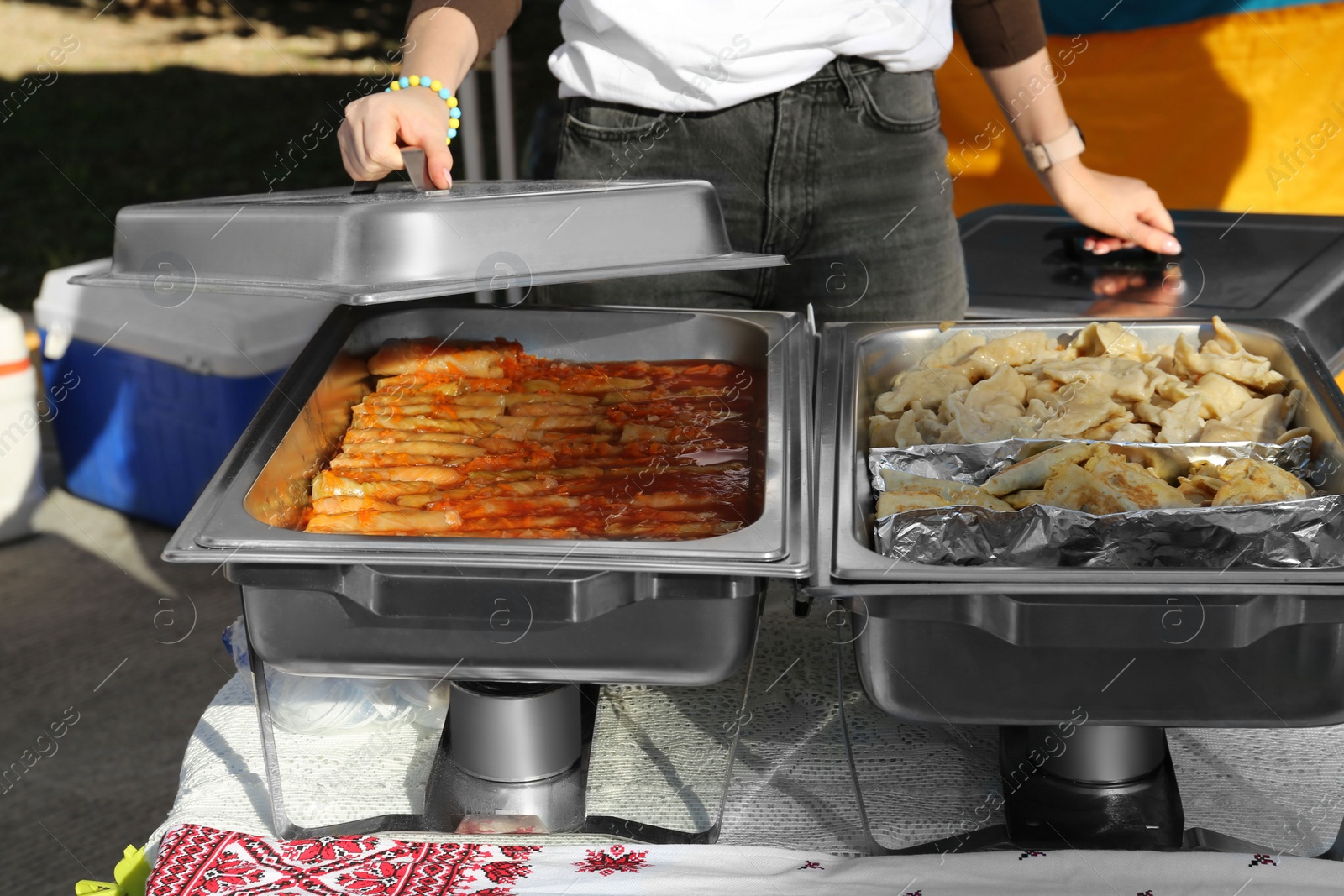 Photo of Female volunteer distributing delicious stuffed cabbage, dumplings and patties from food warmers