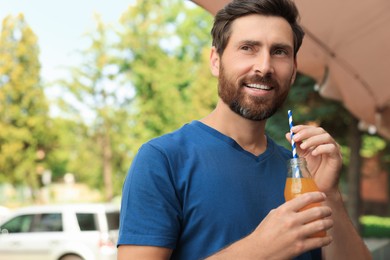 Handsome man with bottle of delicious juice outdoors. Space for text