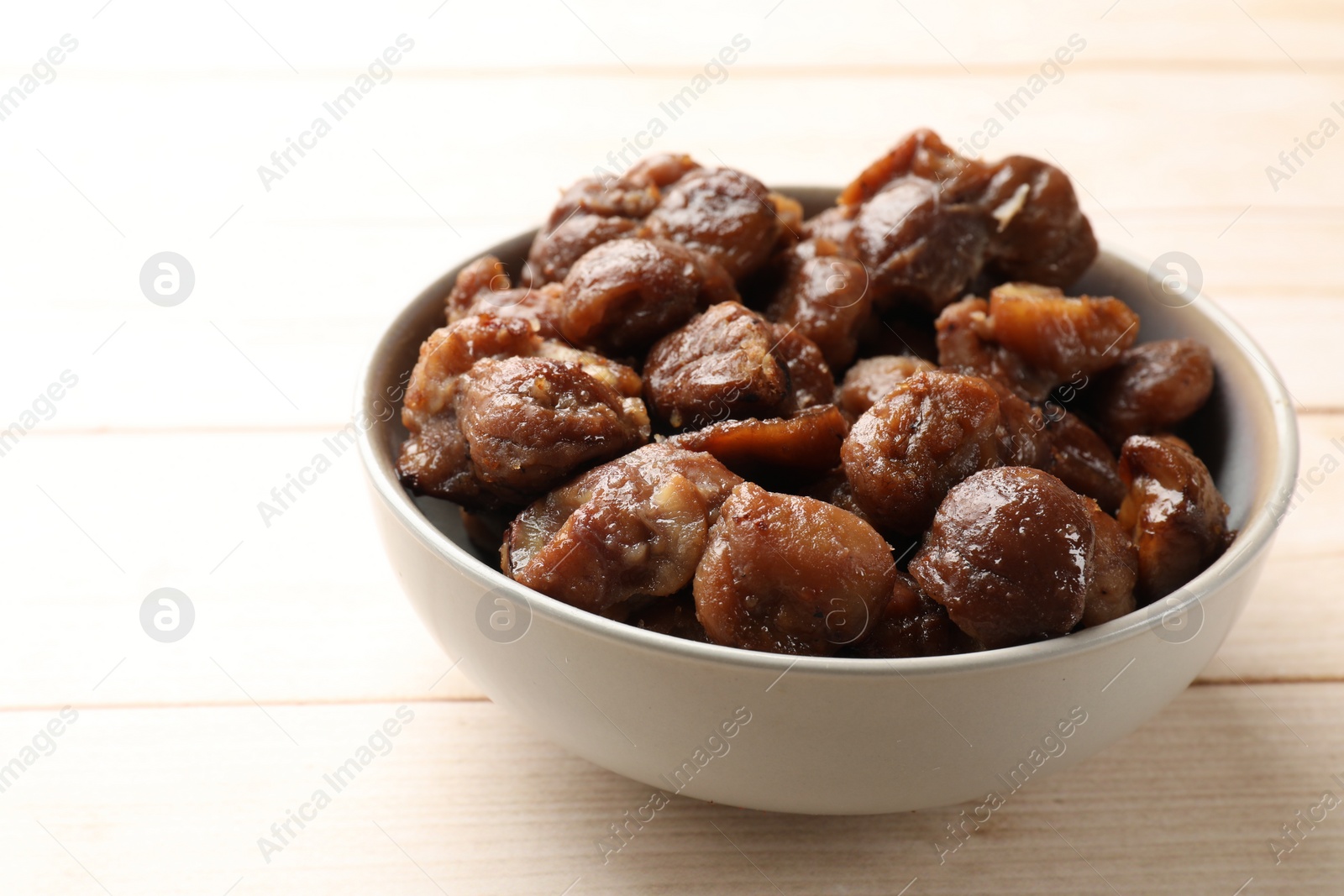 Photo of Roasted edible sweet chestnuts in bowl on light wooden table, closeup