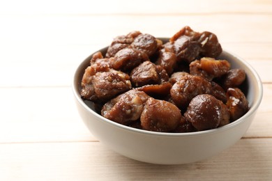 Photo of Roasted edible sweet chestnuts in bowl on light wooden table, closeup