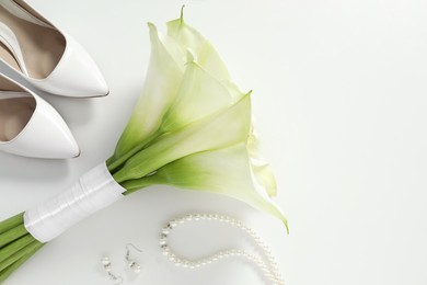 Photo of Beautiful calla lily flowers tied with ribbon, shoes and jewelry on white background, flat lay. Space for text