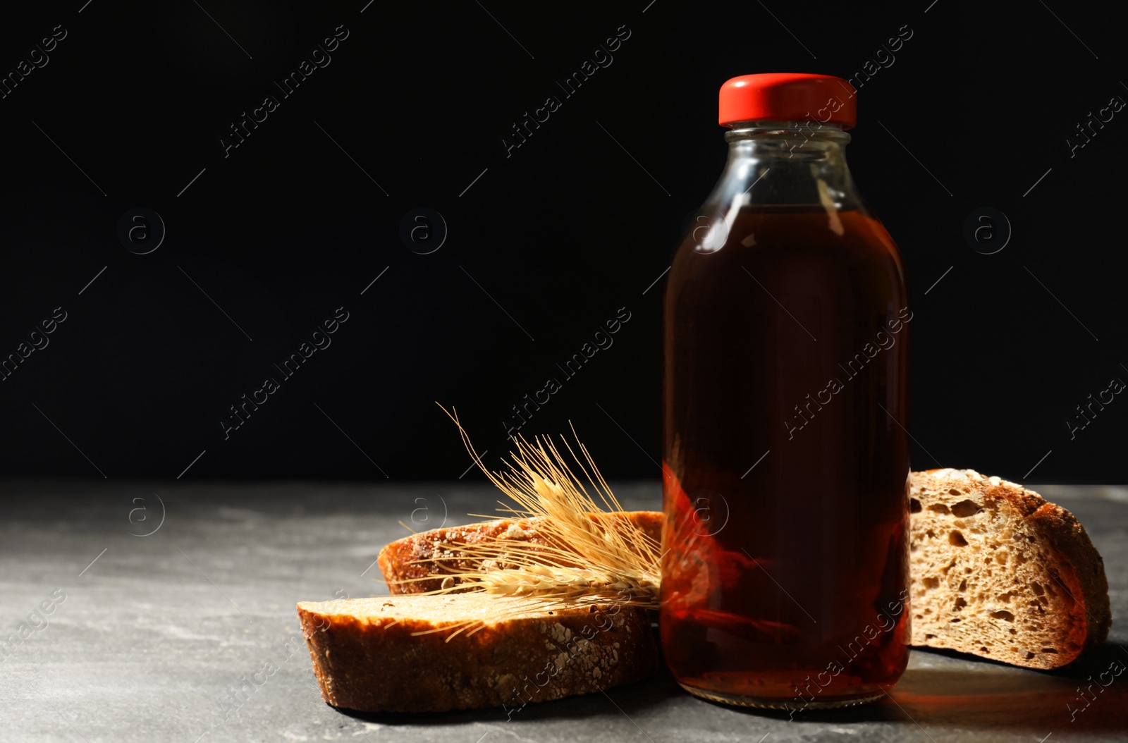 Photo of Bottle of delicious fresh kvass, spikelets and bread on grey table. Space for text