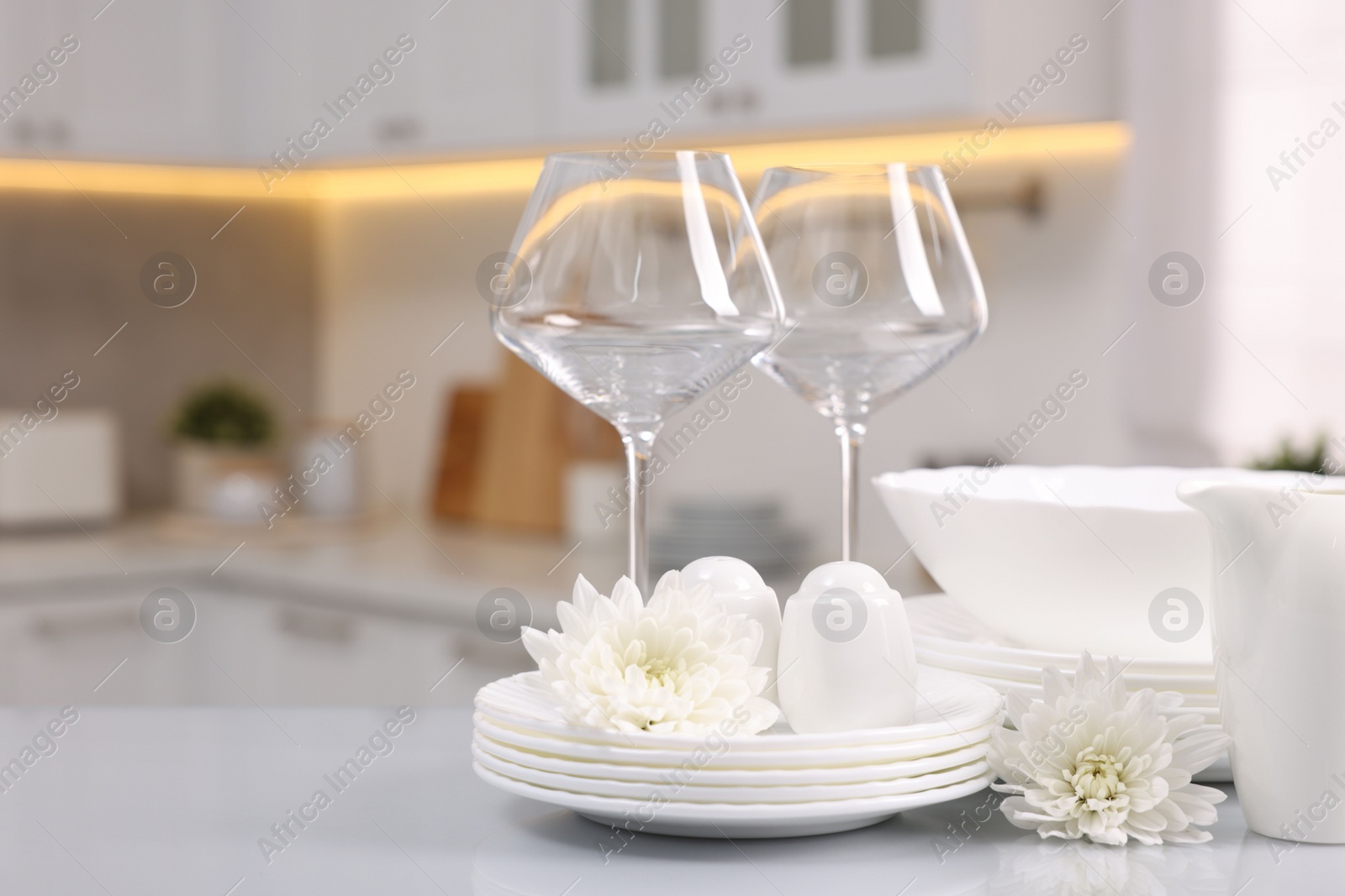 Photo of Set of clean dishware, glasses and flowers on table in kitchen. Space for text