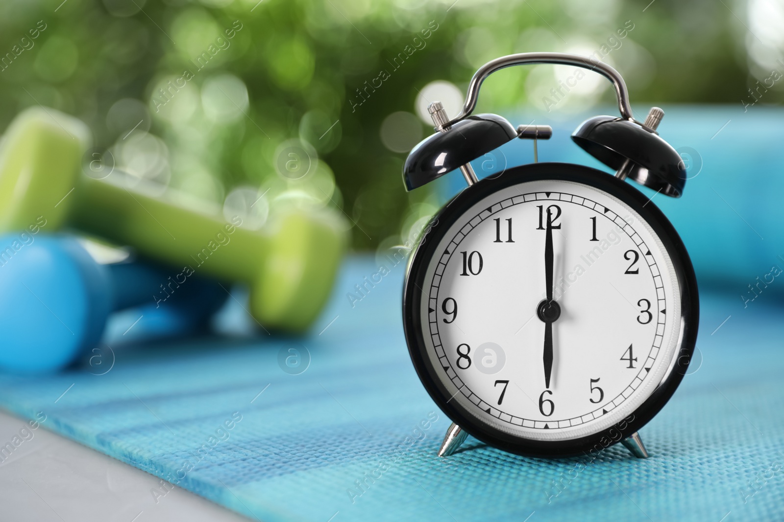 Photo of Alarm clock on yoga mat against blurred background. Morning exercise