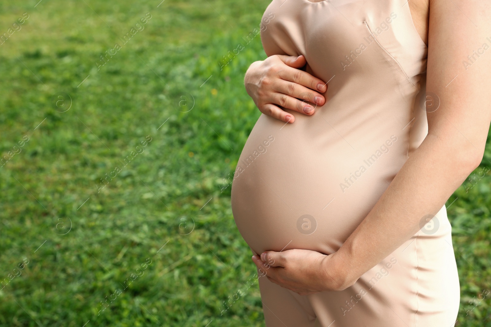 Photo of Pregnant woman touching belly on green grass, closeup. Space for text