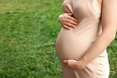 Pregnant woman touching belly on green grass, closeup. Space for text