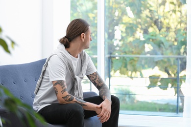 Young man with stylish tattoos at home. Space for text